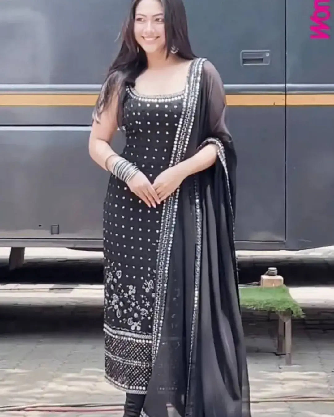 Woman in a black and white traditional outfit standing in front of a bus.