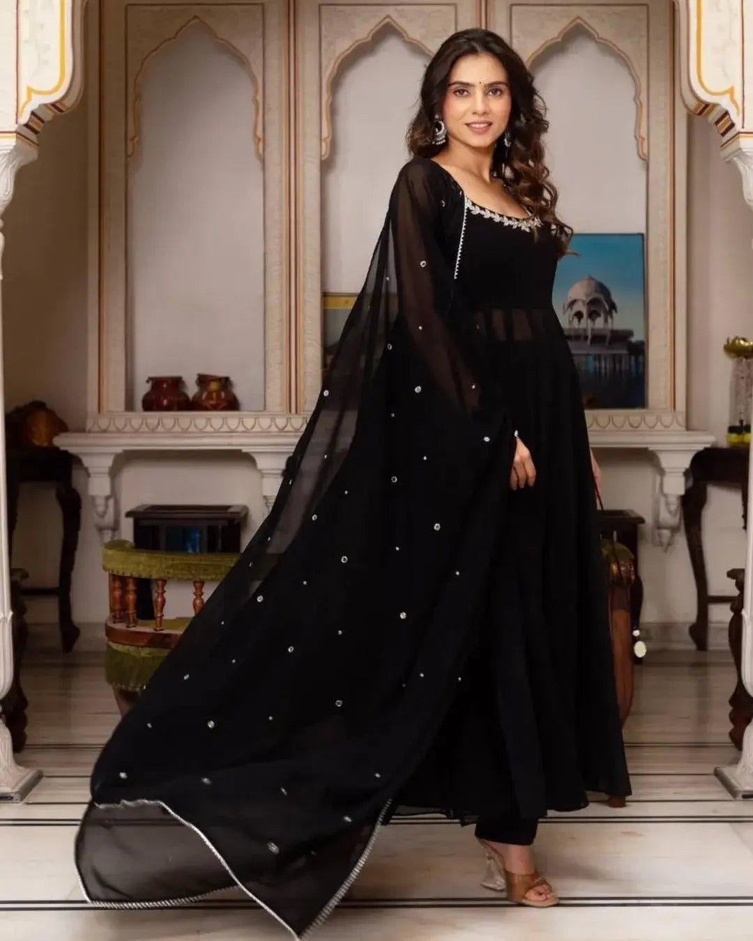 Woman in a black dress with silver embellishments standing in an elegant interior setting.