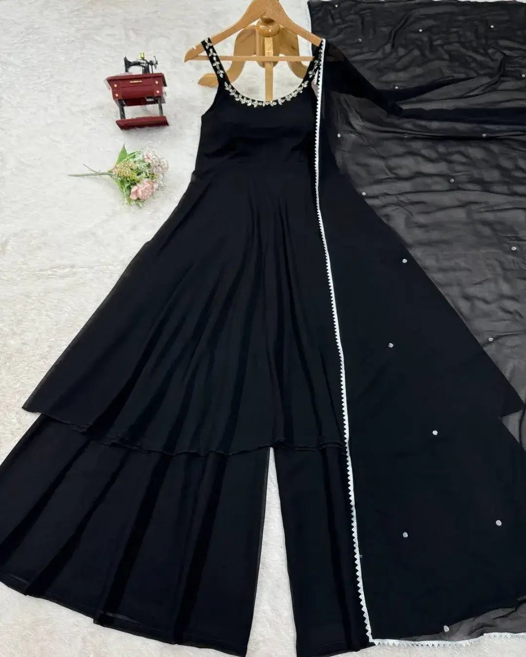 Black dress with white embellishments on a wooden hanger against a textured surface.