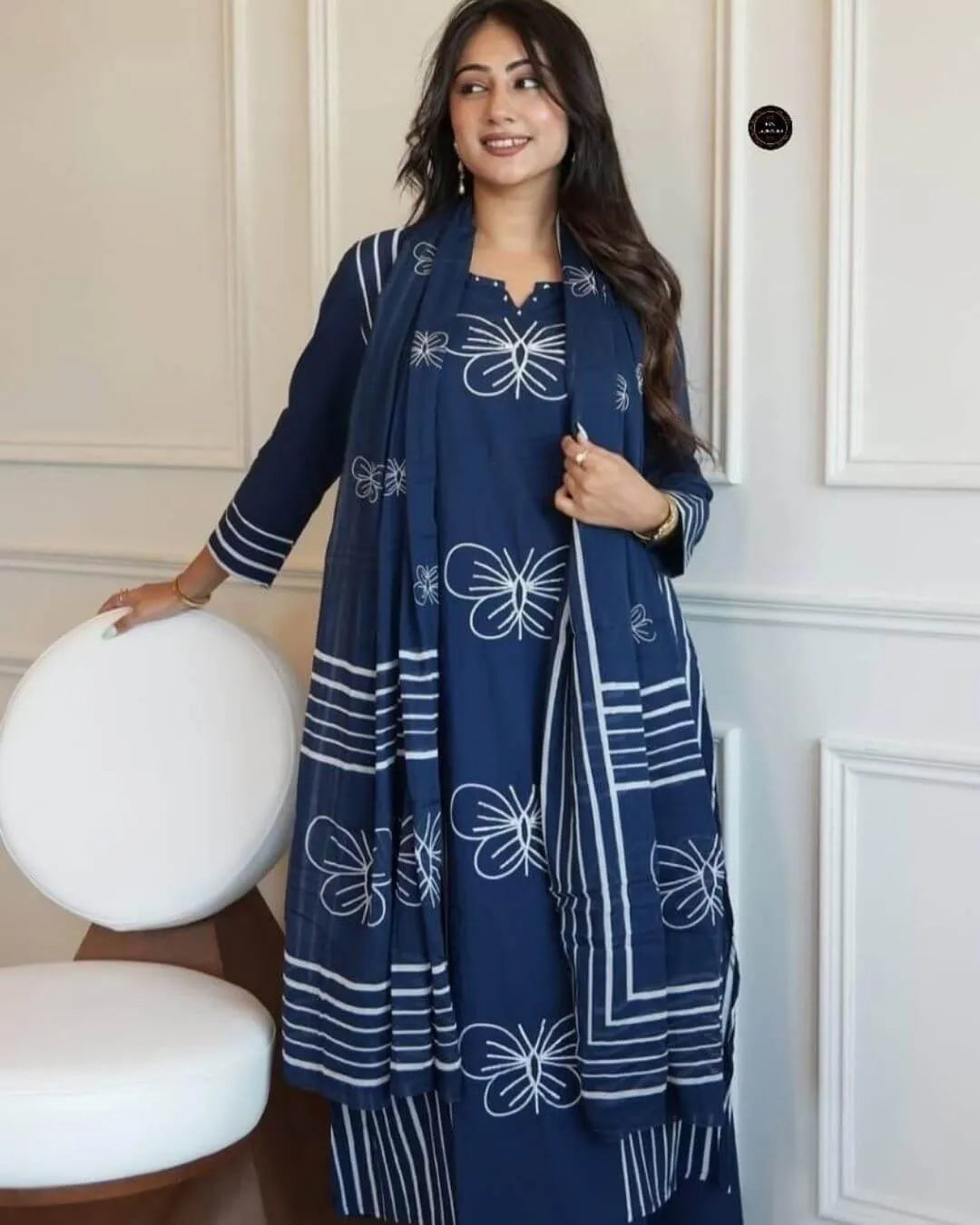 Woman wearing a blue colour suit set with dupatta outfit with white patterns in a room with white walls and furniture.