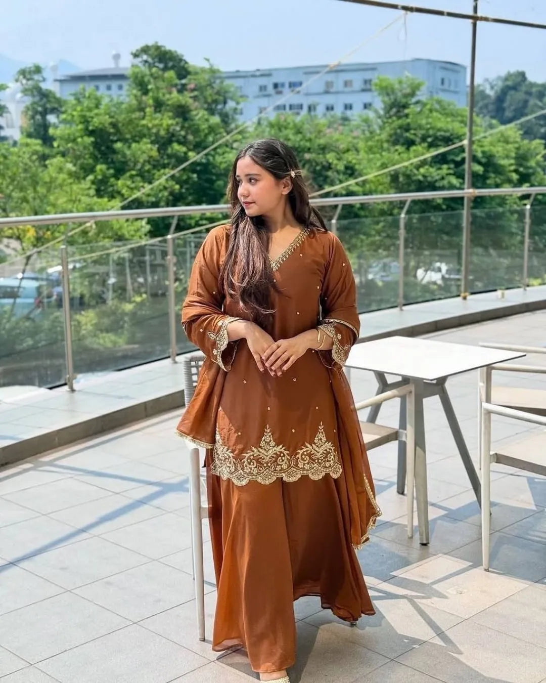 Woman wearing a brown sharara dress in an indoor setting with decorative elements.