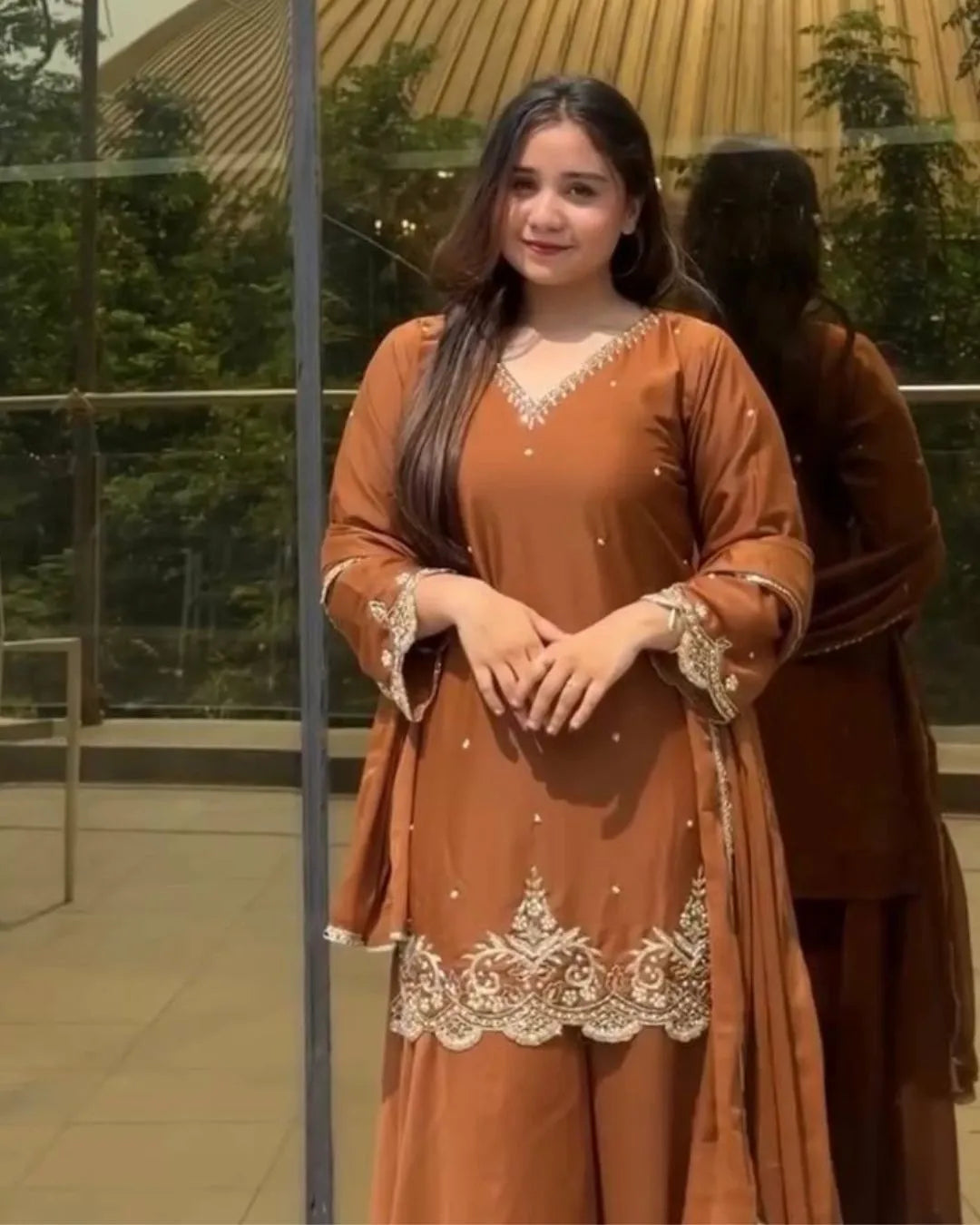 Woman wearing a brown traditional outfit with intricate white embroidery in an outdoor setting.