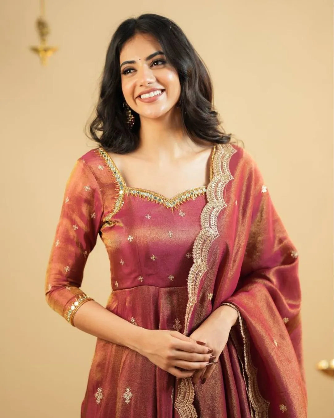 Woman wearing a traditional maroon and gold saree with a beige background