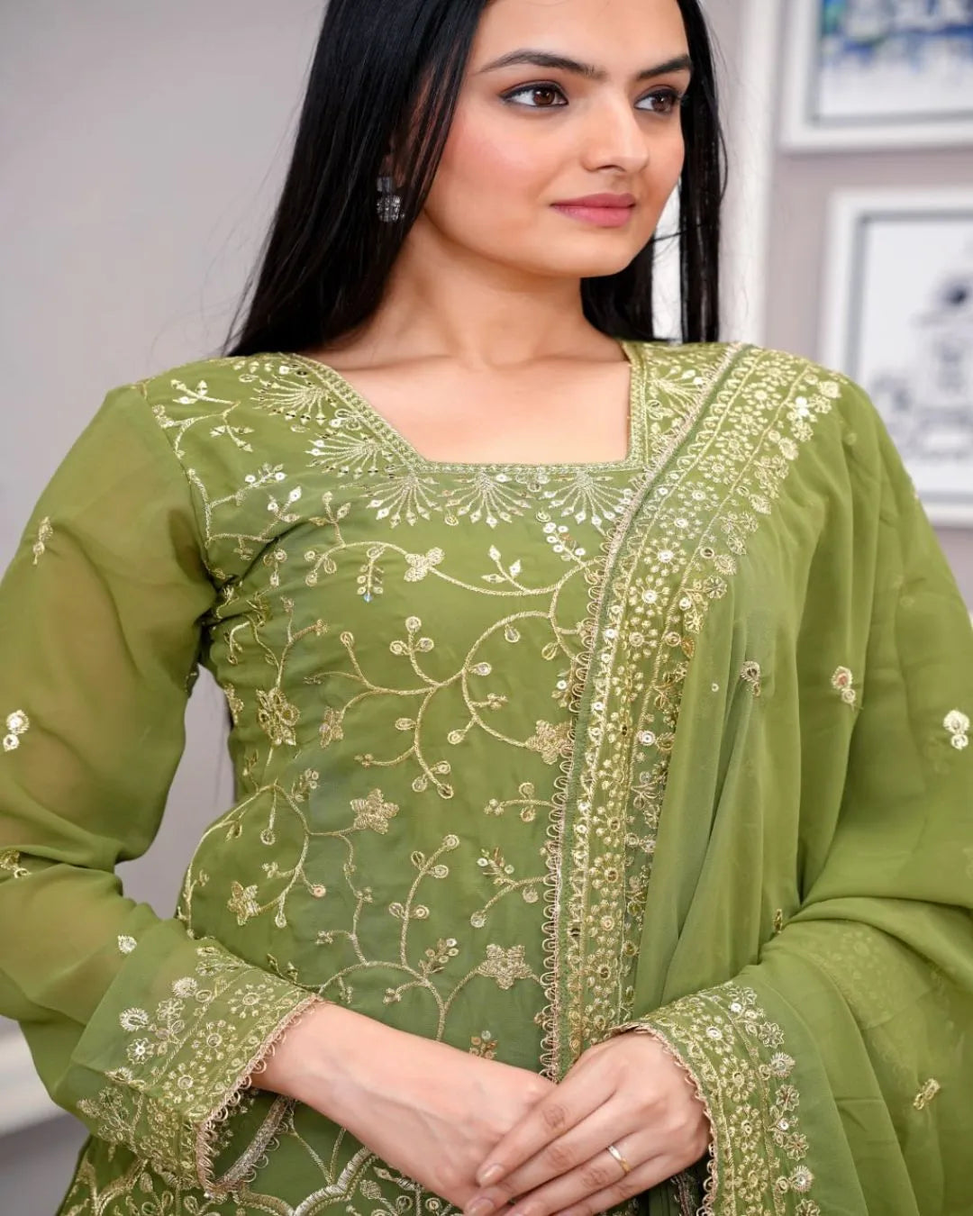 Woman wearing a green embroidered traditional outfit indoors.
