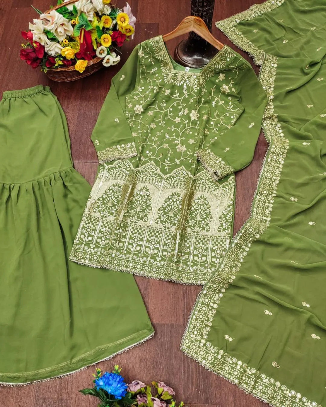 Green embroidered traditional outfit with matching dupatta on a wooden surface.