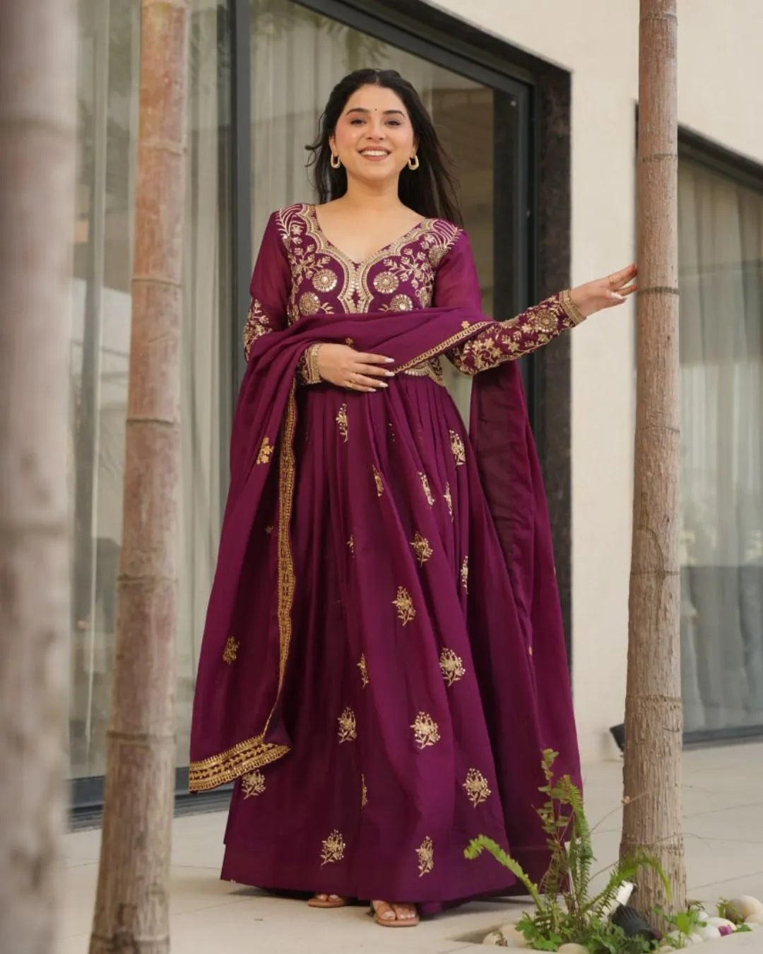 Woman in a purple traditional outfit with gold embroidery standing outdoors.