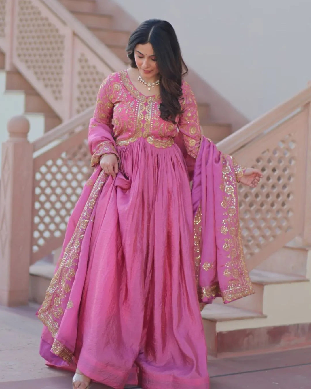 Woman in a traditional pink and gold outfit standing on a staircase.