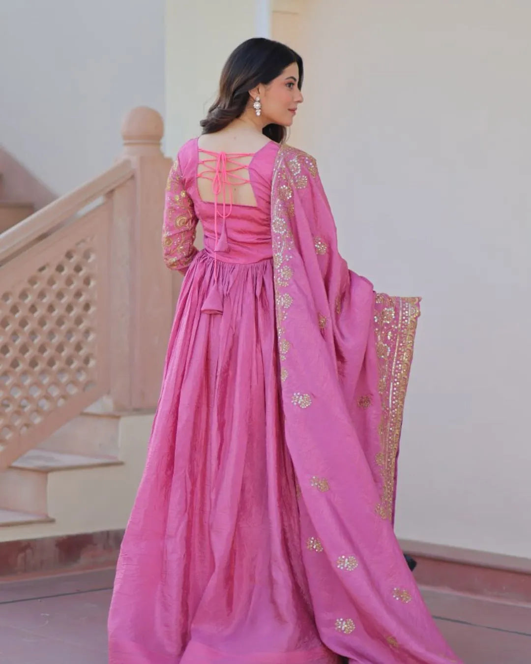 Woman in a pink traditional outfit with a decorative dupatta, standing indoors.
