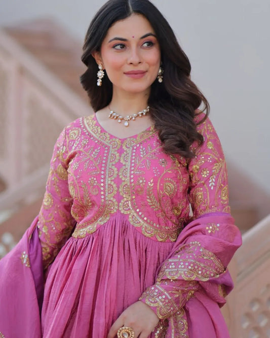 Woman wearing a pink traditional outfit with gold embroidery indoors.