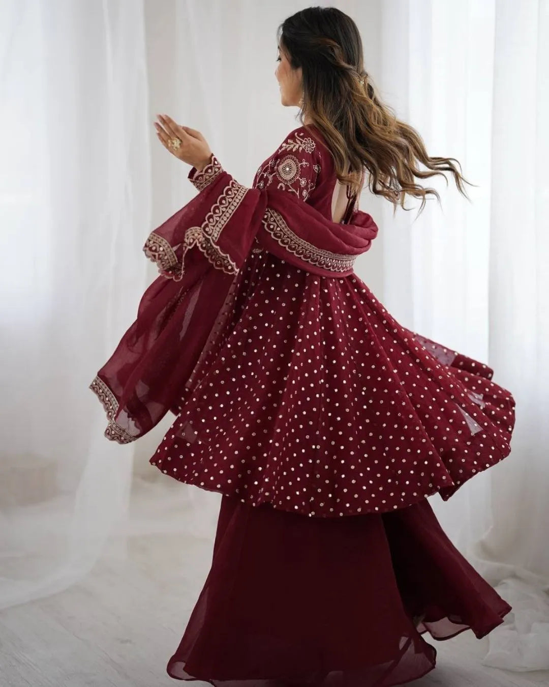 Woman wearing a maroon dress with intricate embroidery in a softly lit room.