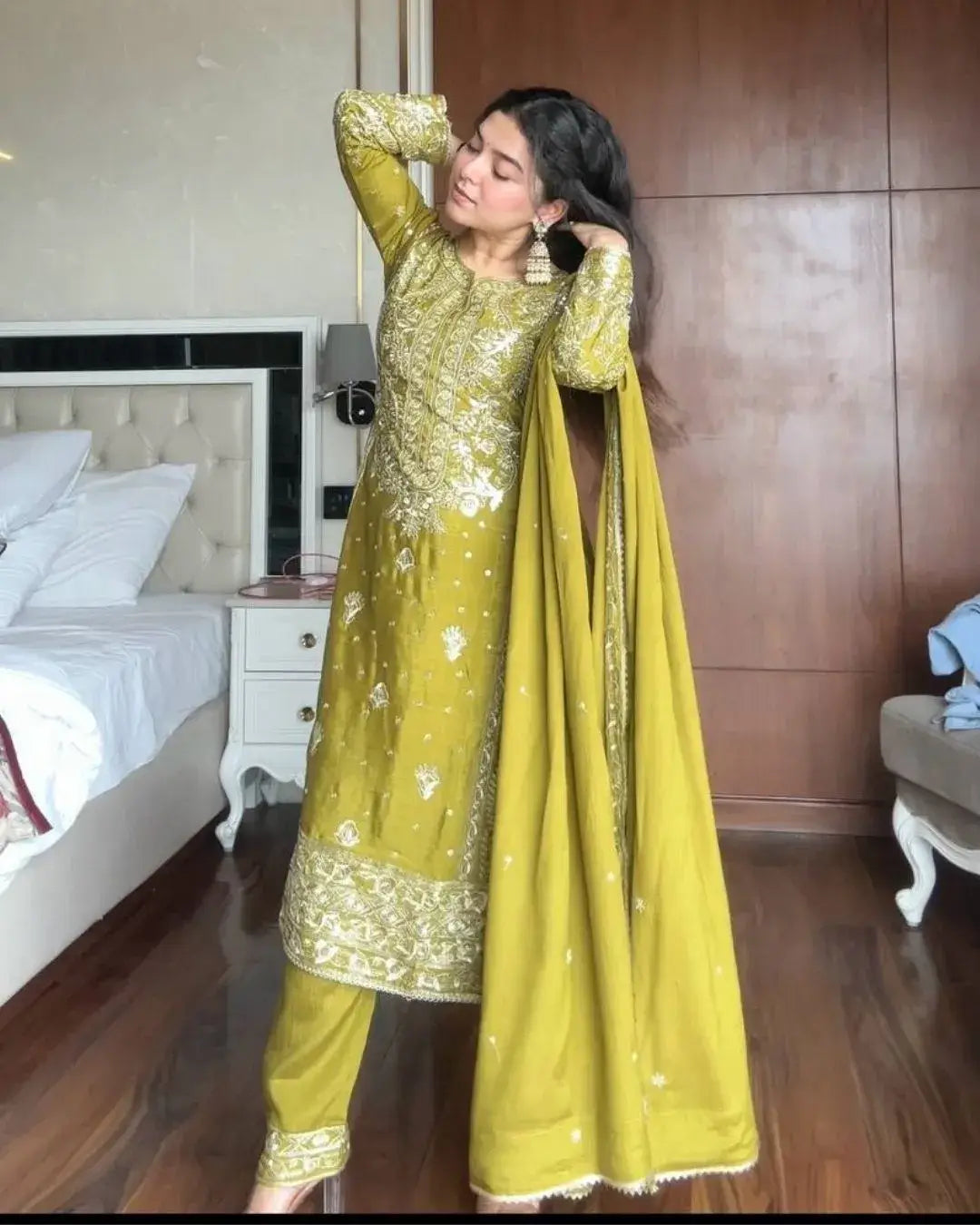 Woman in a yellow traditional outfit standing in a bedroom.