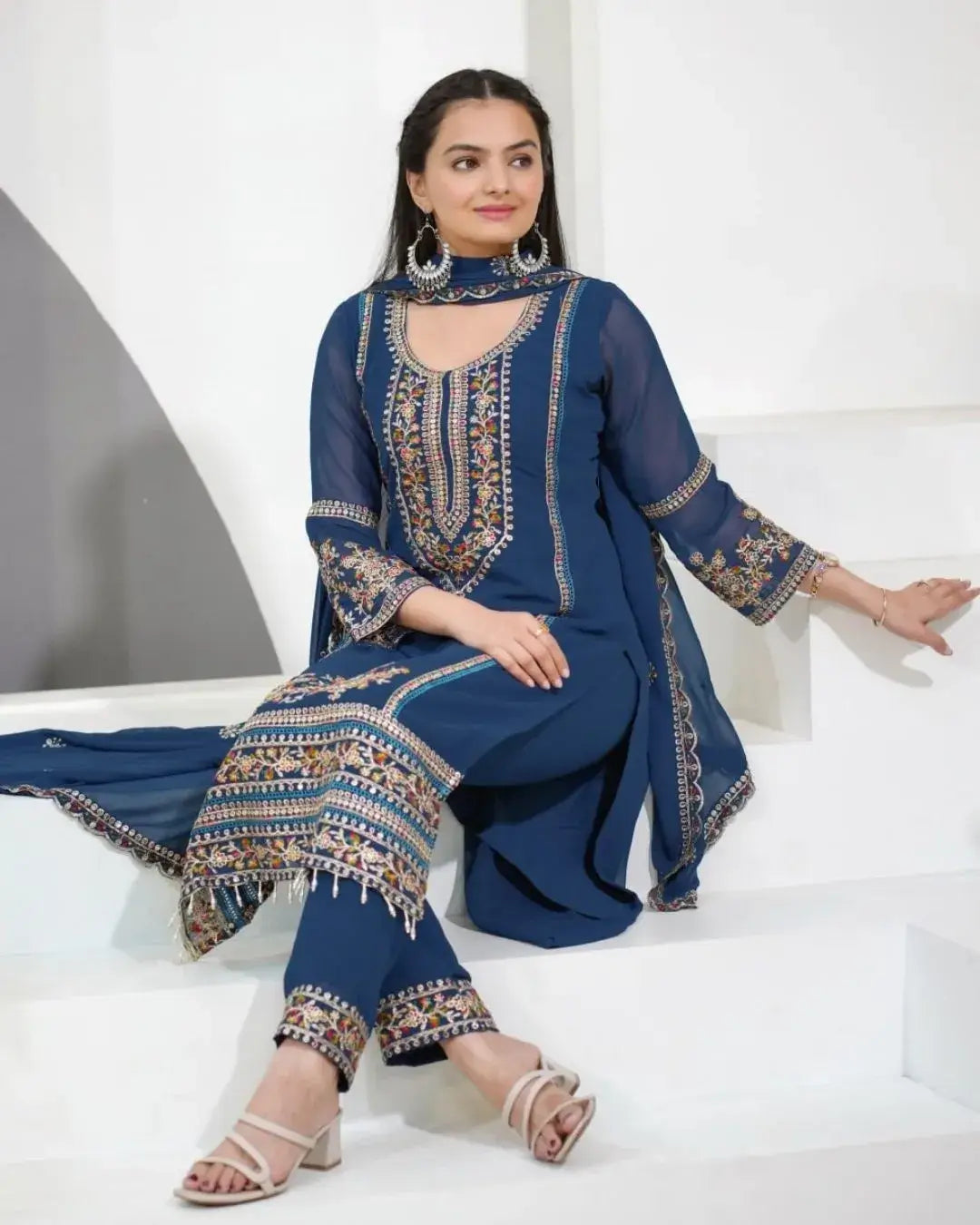 Woman wearing a blue embroidered outfit sitting on a white surface.