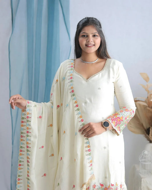 Woman wearing a white traditional outfit with floral patterns in a room with light blue curtains.