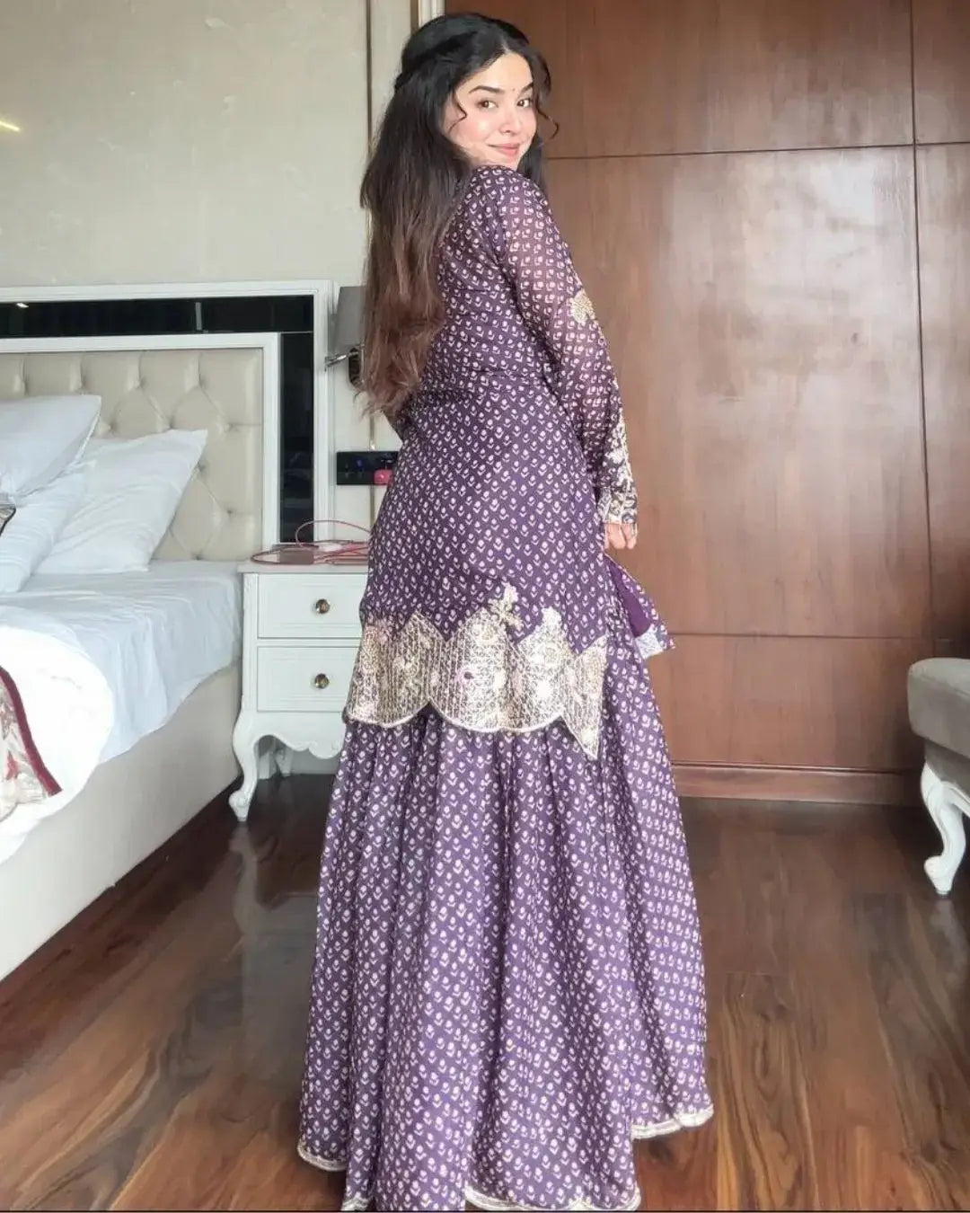 Woman in a purple traditional outfit standing in a bedroom.