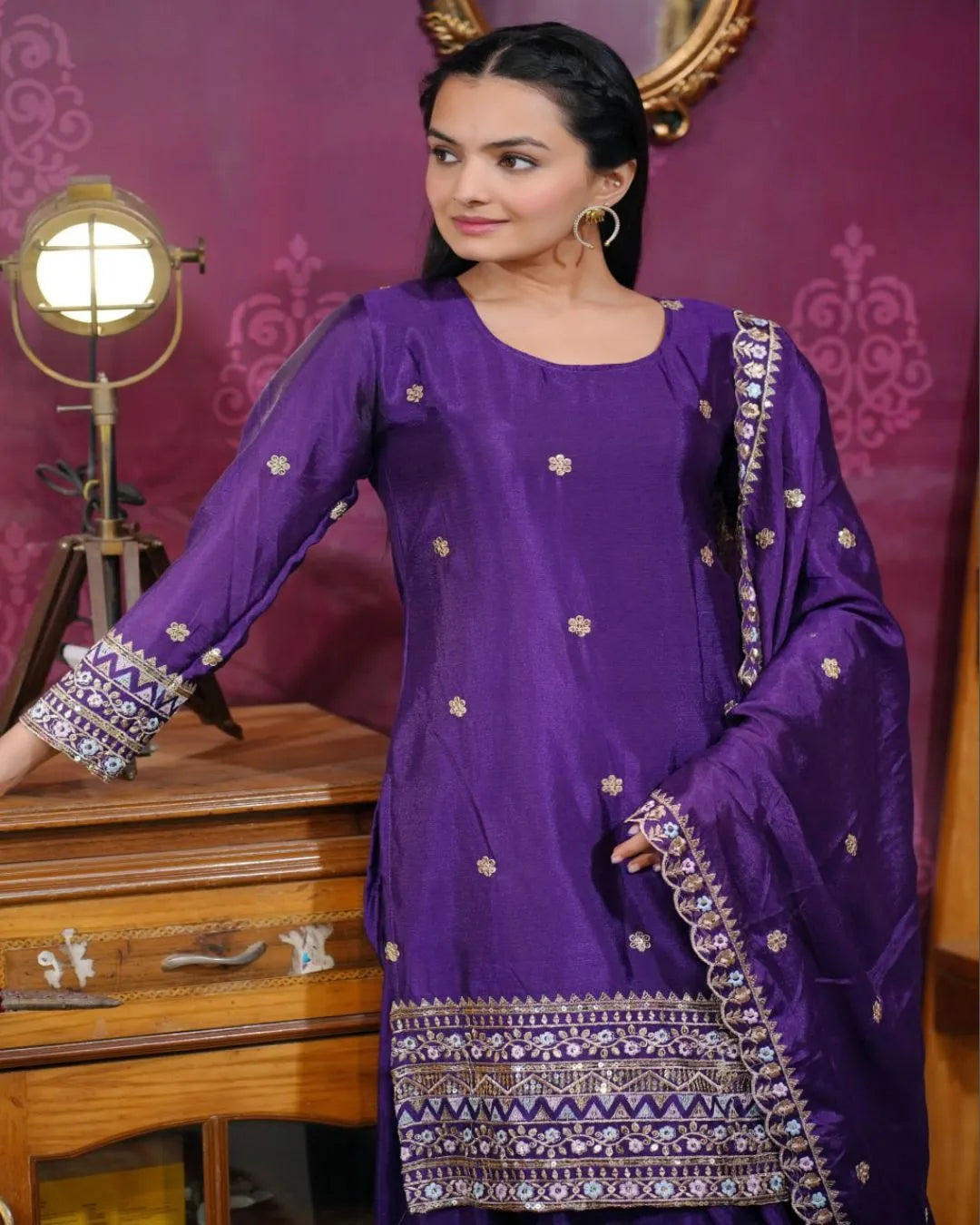 Woman wearing a purple traditional outfit with intricate patterns in a decorative setting.