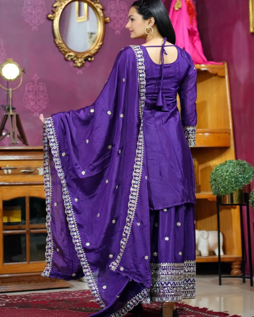 Woman wearing a purple traditional outfit with silver details in a decorated room.