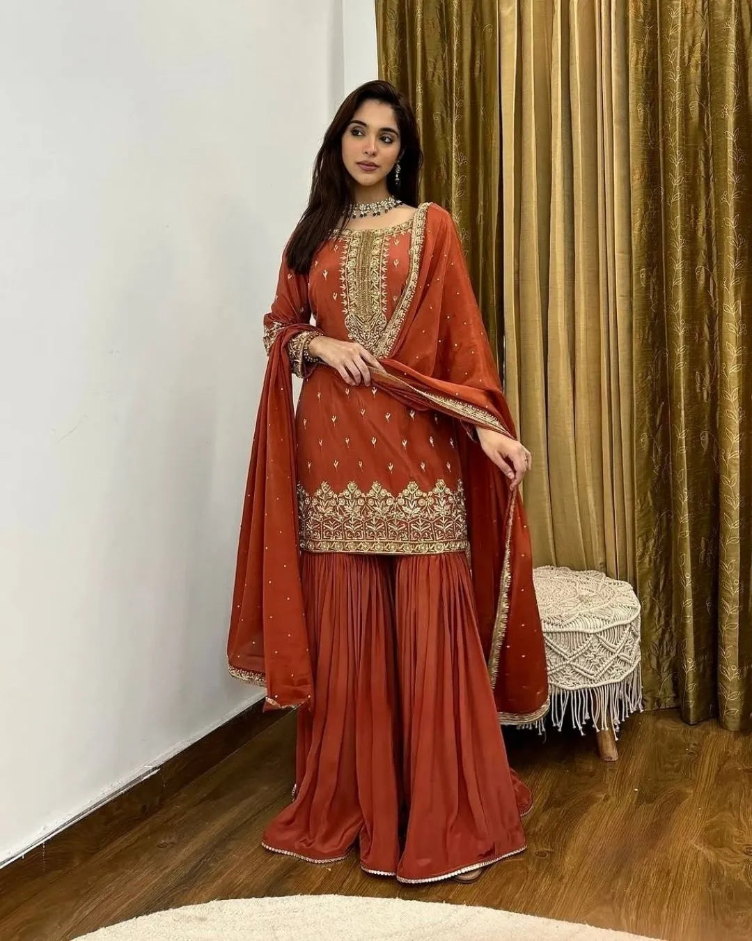 Woman in a orange traditional outfit with a dupatta indoors.