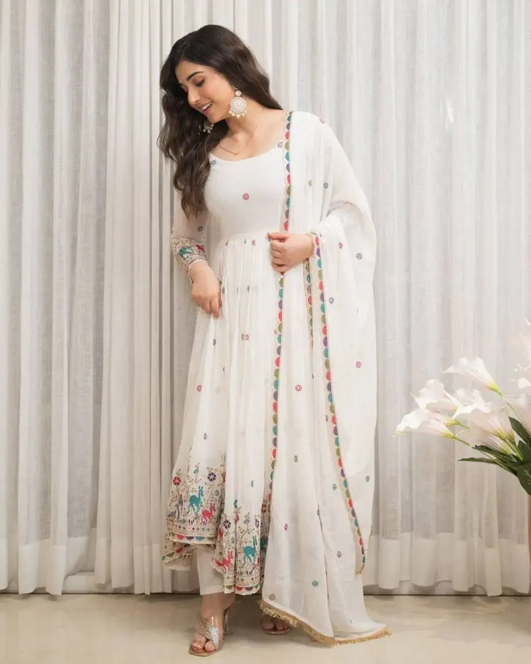 Woman in a white traditional outfit with floral patterns against a light curtain background