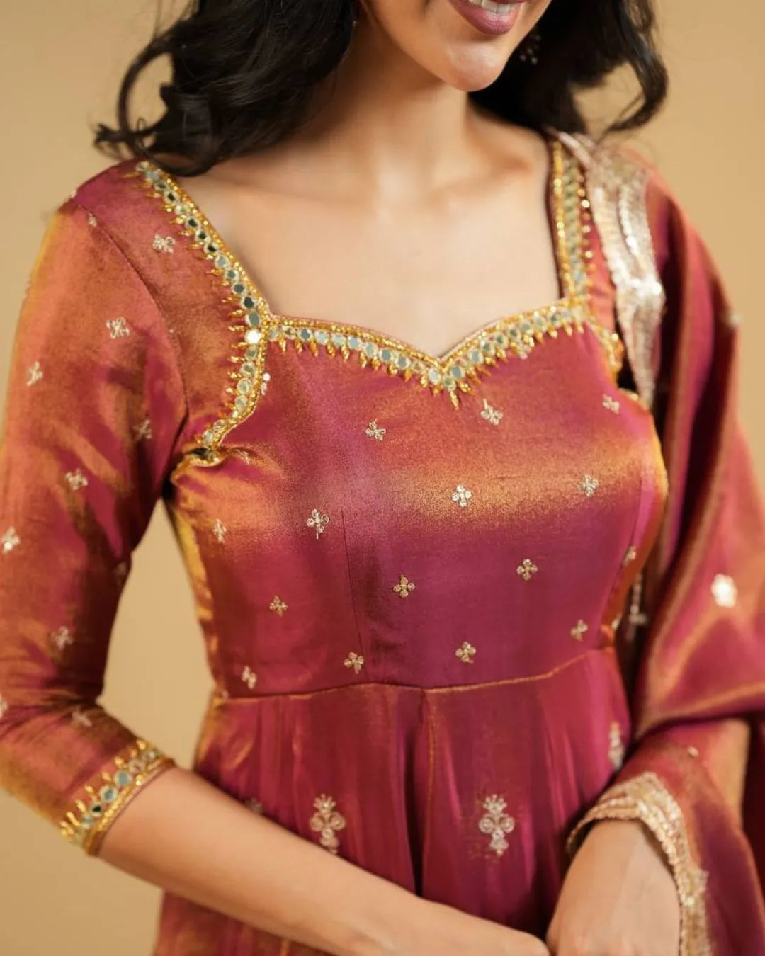 Woman wearing a traditional maroon and gold embroidered dress against a beige background