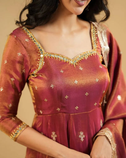 Woman wearing a traditional maroon and gold embroidered dress against a beige background