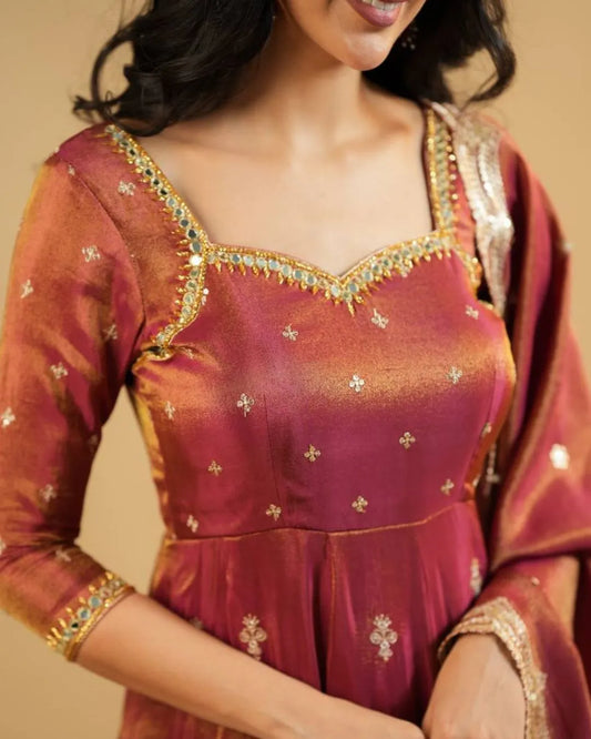 Woman wearing a traditional maroon and gold embroidered dress against a beige background