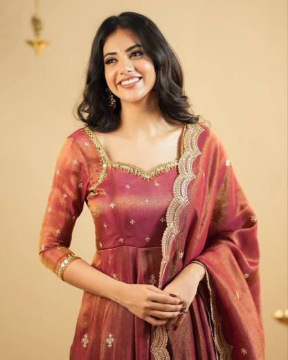 Woman wearing a traditional maroon and gold saree with a beige background