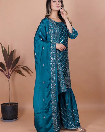 Woman wearing a teal traditional outfit with intricate patterns against a beige background