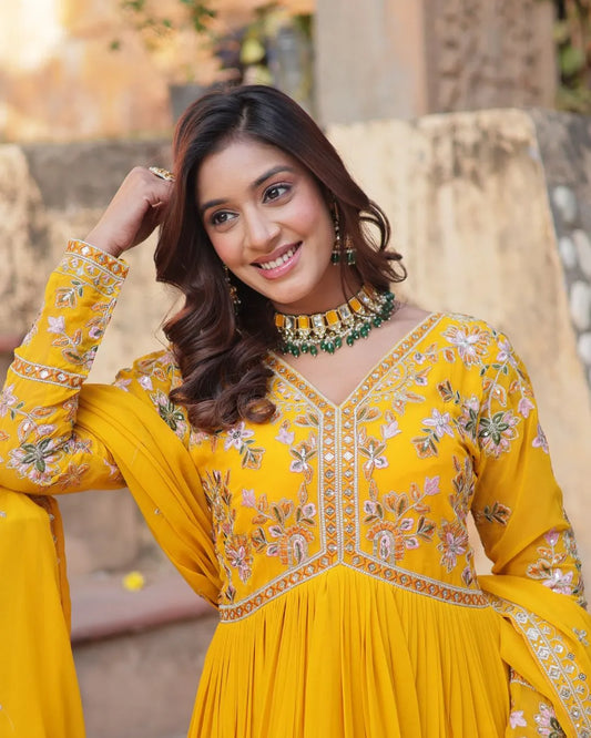 Woman wearing a yellow embroidered outfit with floral patterns outdoors.