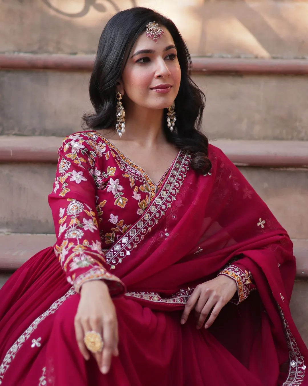 Woman in a red traditional outfit with intricate patterns sitting on steps.