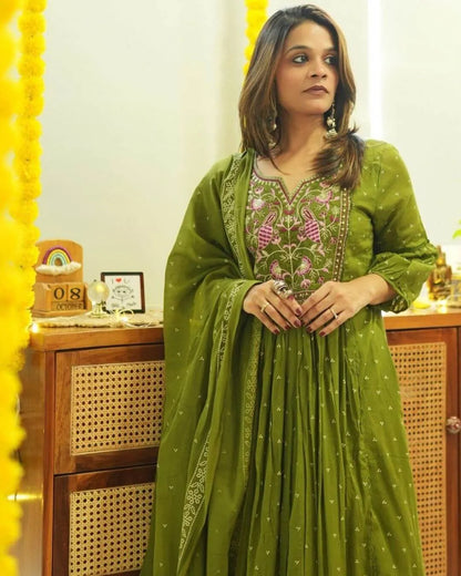 Woman in a green embroidered dress standing in a decorated room.