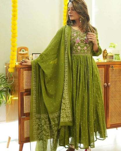 Woman wearing a Green Colour Anarkali Suit Set outfit with a matching dupatta in a room.