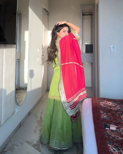 Woman in a green suit with a pink dupatta standing in a room.