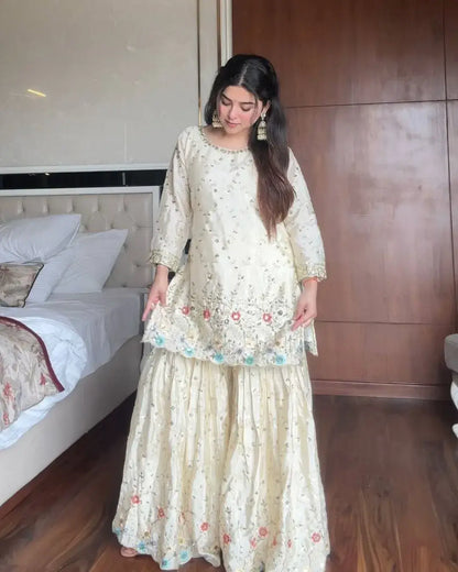 Woman in a light-colored traditional outfit standing in a bedroom.