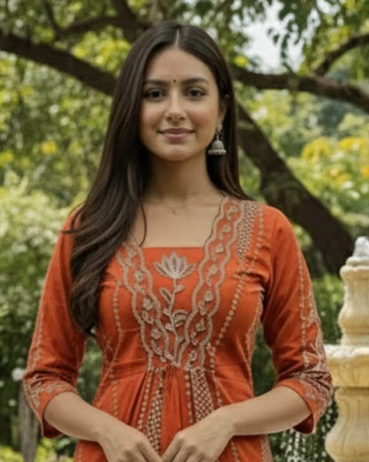 Woman in an orange cotton A-Line suit set traditional outfit standing in a garden with a fountain.