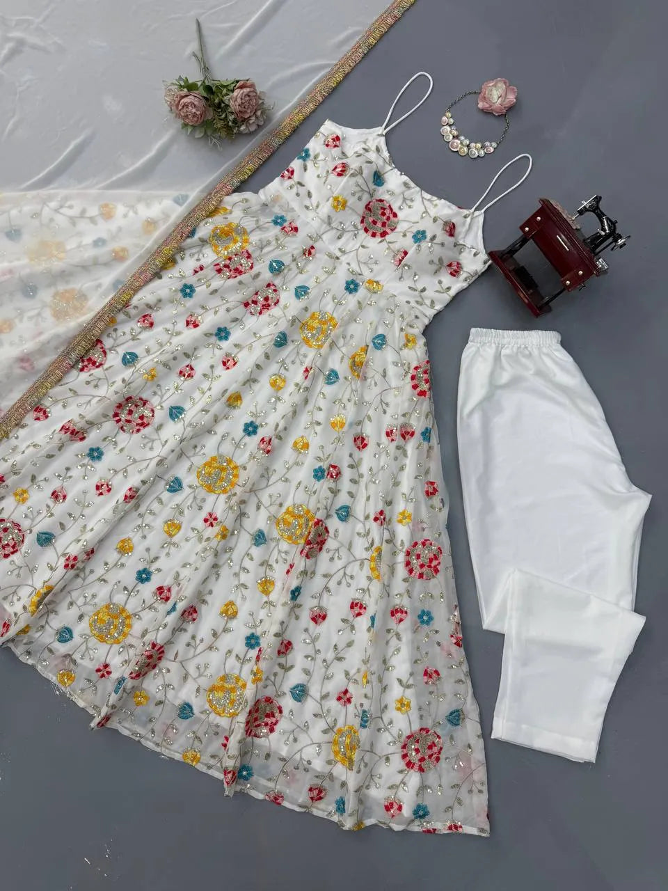 Floral dress with colorful flowers and white pants on a gray surface.