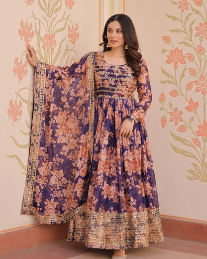 Woman wearing a floral dress with a matching dupatta against a decorative wall.
