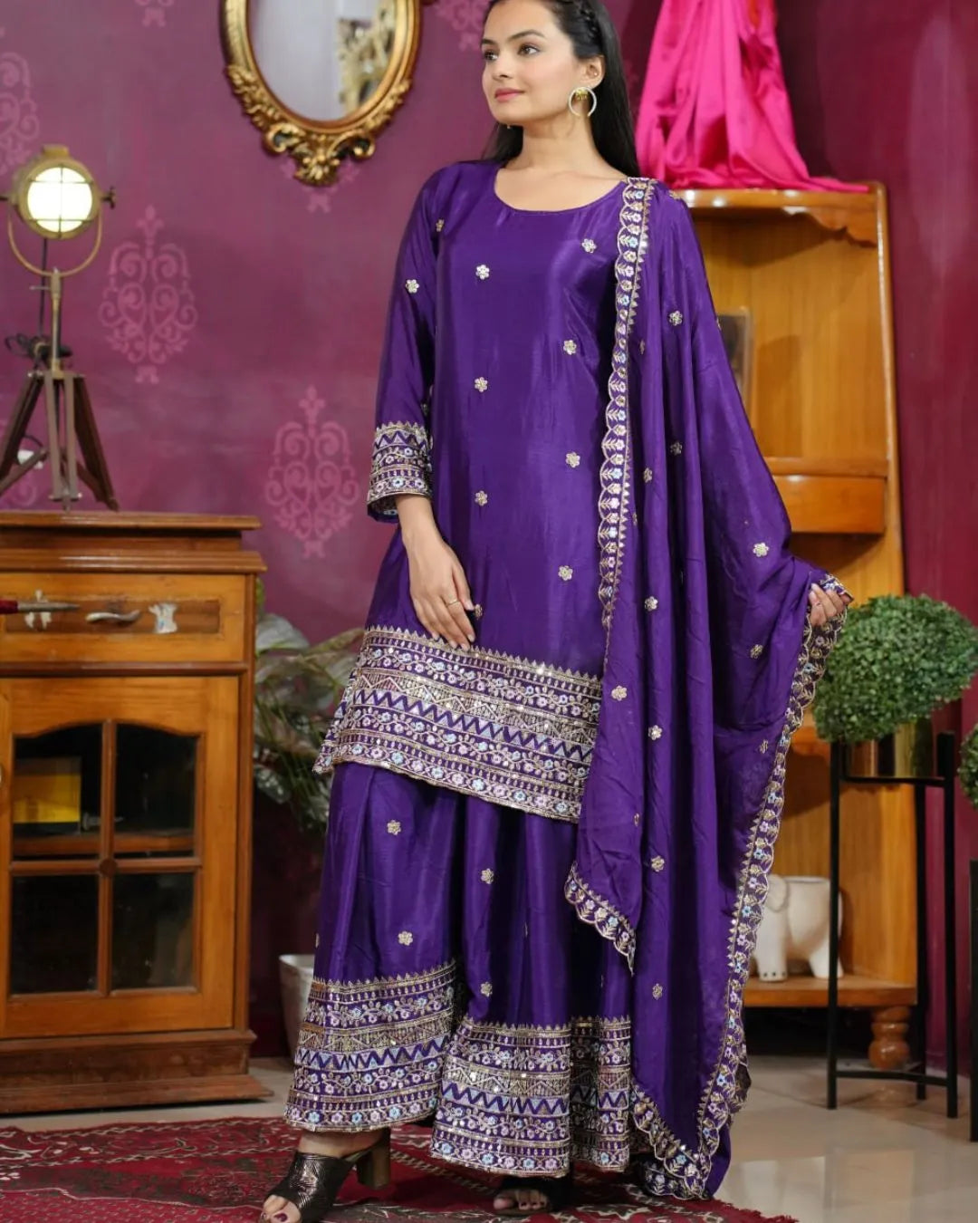 Woman in a purple traditional outfit with silver patterns in a decorated room.