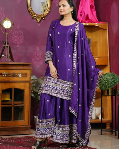 Woman in a purple traditional outfit with silver patterns in a decorated room.
