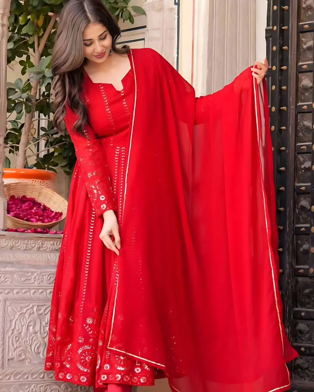 Woman wearing a red traditional outfit with a matching dupatta, standing indoors.