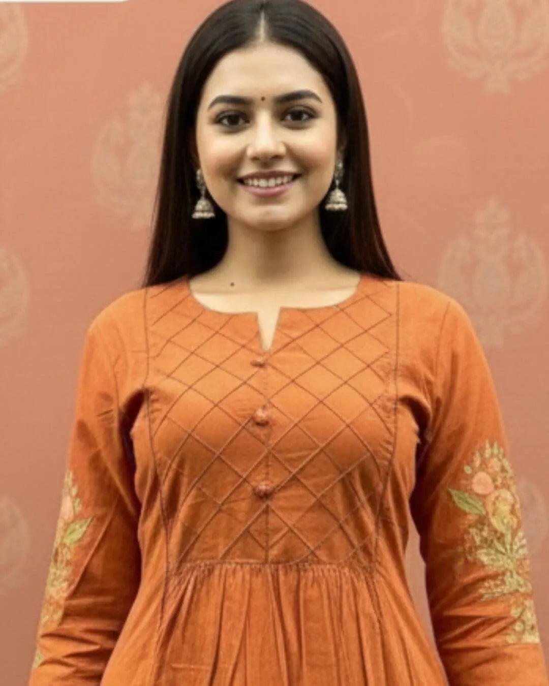 Woman wearing an orange cotton kurti pant dupatta set outfit with a patterned background